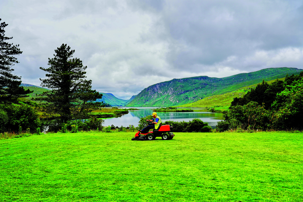 Eine Person auf einem Rasenmähtraktor vor idyllischer Kulisse
